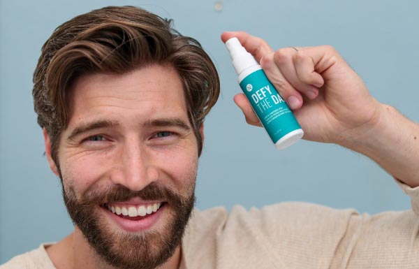 A man holding up the Defy the Day Leave-in Conditioner Spray bottle.