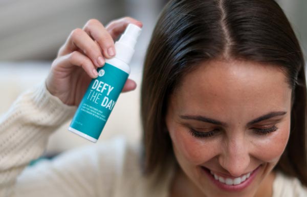 A woman holding up a bottle of the Defy the Day Leave-in Conditioner Spray.