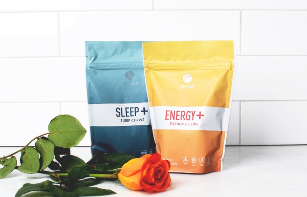 Lifestyle shot of Sleep+ Energy+ Wellness Chews Combo sitting on a white counter with a rose in front of it.
